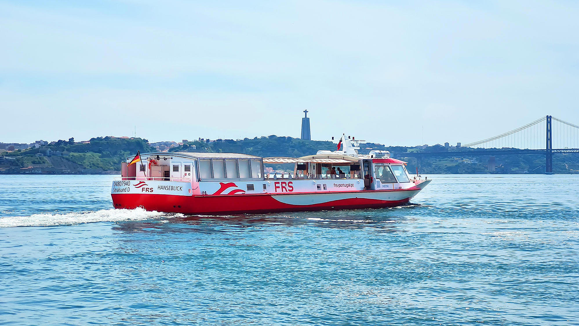 Vessel cruising on the Tagus river, Cristo Rei and the Ponte 25 de Abril in the background.