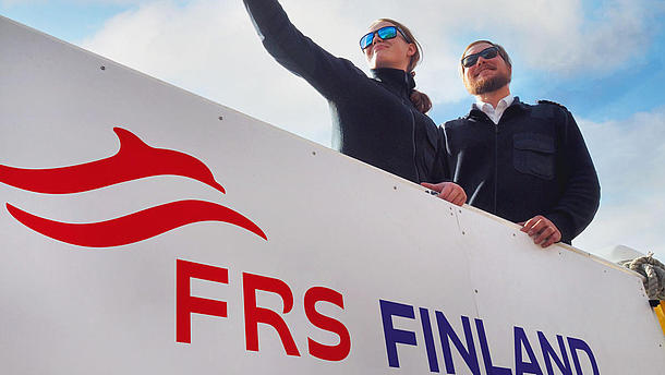 Two crew members of FRS Finland aboard a vessel; a woman on the left showing something to a man on the right.