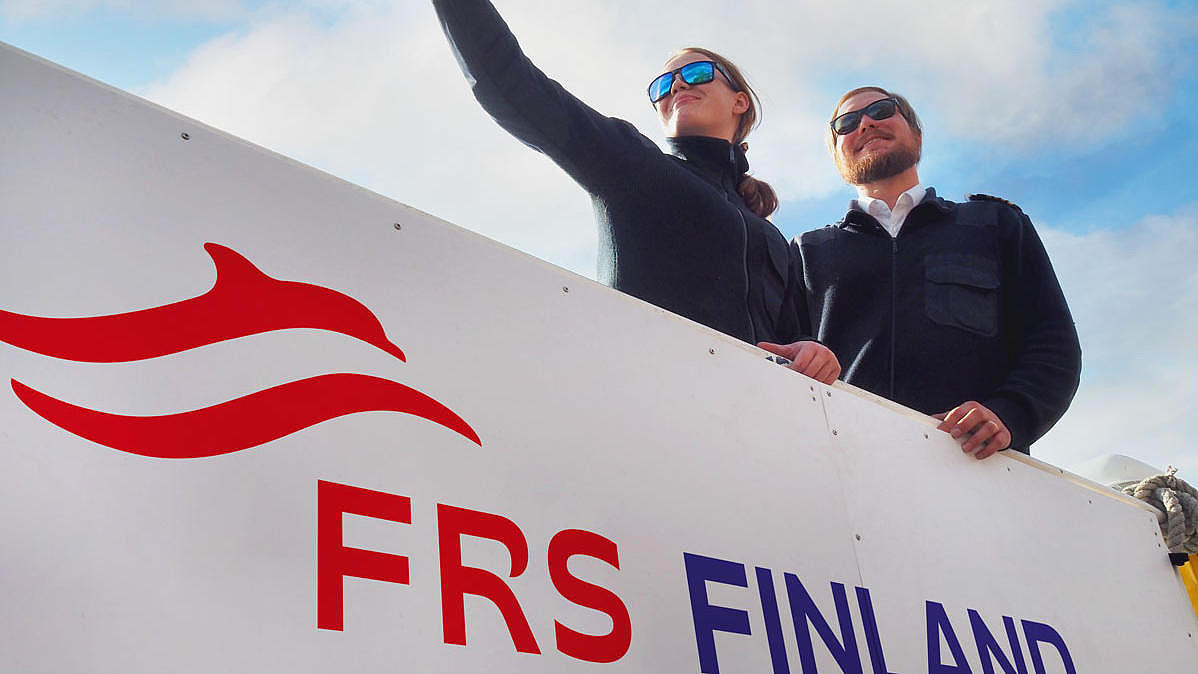 Two crew members of FRS Finland aboard a vessel; a woman on the left showing something to a man on the right.