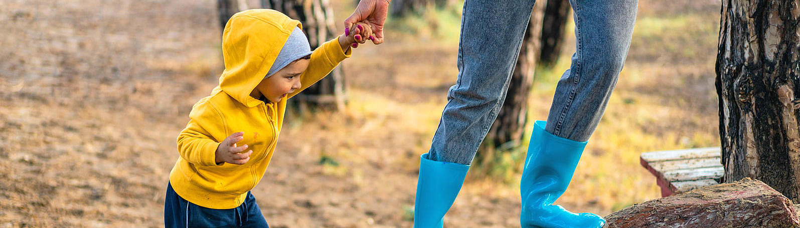 An adult, is helping a child to get up a wood stump.