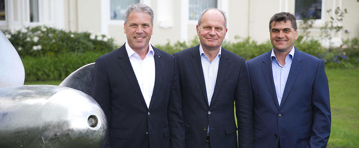 The CEOs of FRS next to a ship's propeller.