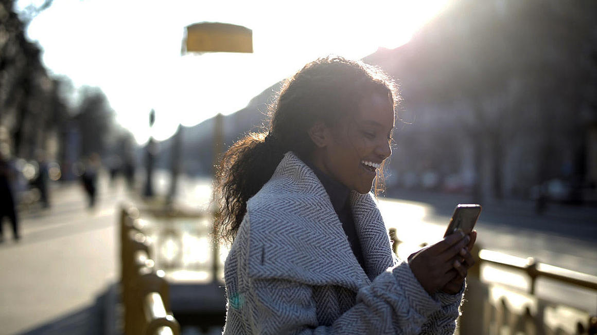 EIne Frau die ihr Handy hält und dabei lacht.