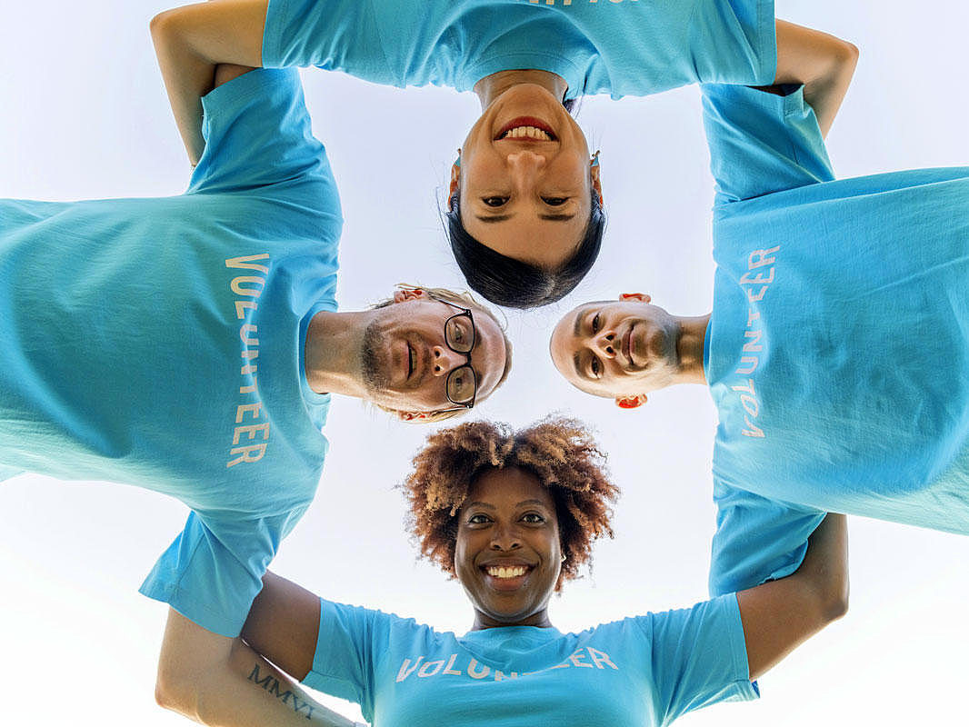 Vier Ehrenamtlichen, die einen Kreis aus Menschen formen. 